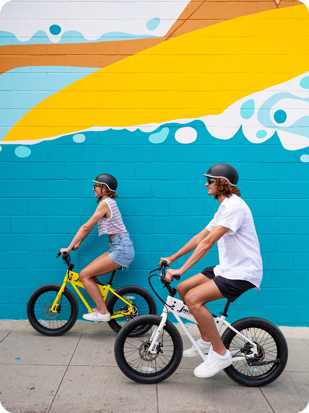 Two riders on JackRabbits in front of a colorful mural